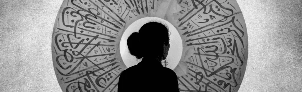 kobieta stojąca przed kołem, na którym znajdują się artystyczne napisy w alfabecie arabskim, kierunek wschód, język arabski