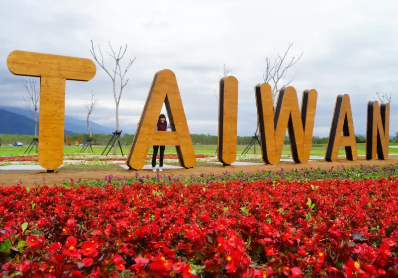 napis Tajwan w ogrodzie, czerwone kwiaty, osoba robiąca sobie zdjęcie przy napisie Taiwan, link do kursu języka chińskiego w Kierunek Wschód