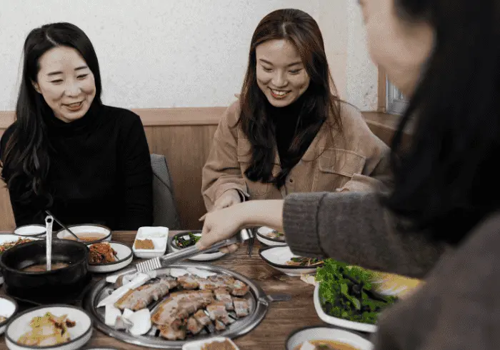 Koreańczycy jedzący różnorodne dania kuchni koreańskiej, takie jak marynowane warzywa i tradycyjne przystawki, podkreślające smakowitą różnorodność koreańskiej kuchni.